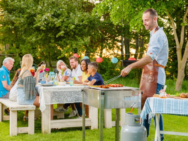 Man aan het barbecueën met familie aan tafel op de achtergrond