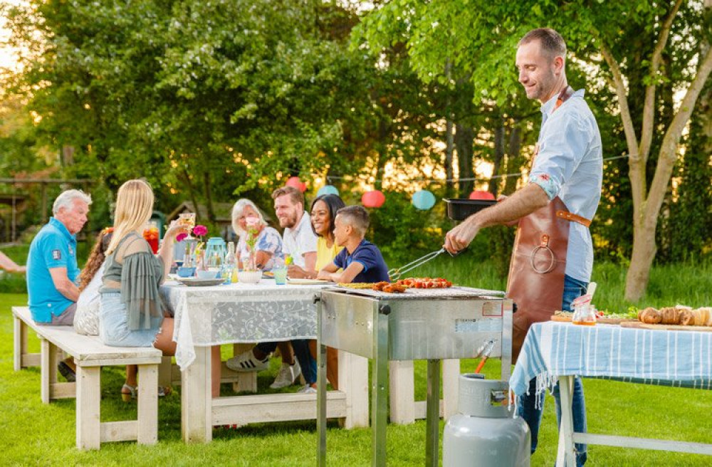 Man aan het barbecueën met familie aan tafel op de achtergrond